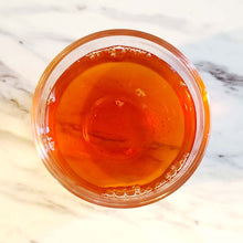 Load image into Gallery viewer, Brewed Royal Cream Earl Grey tea in a clear glass, showcasing rich amber color on a marble surface.